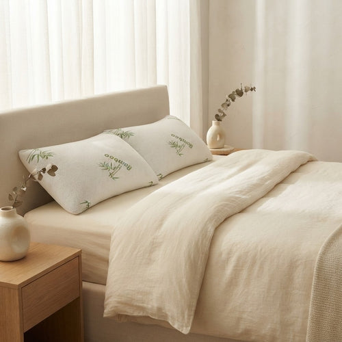 Two bamboo pillows on a made bed with cream linen bedding