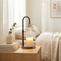 A glass candle warmer lamp on an oak nightstand beside a made bed